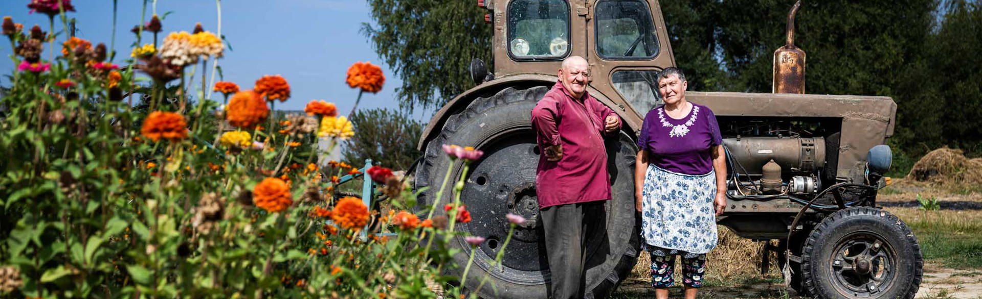 Двоє місцевих жителів позують на своєму городі на фоні трактора