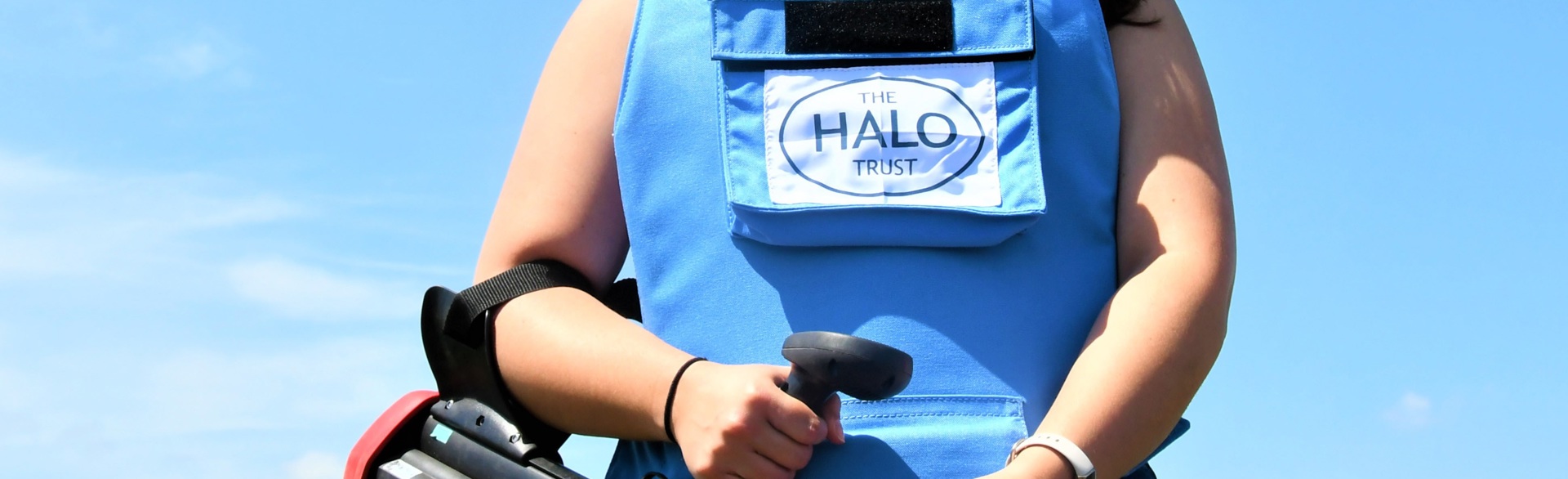 A close up of a person in a HALO vest holding a landmine detector