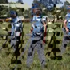 Демінери в захисному спорядженні з детекторами проводять розмінування у високій траві на фоні стіни дерев