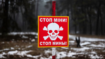A red danger mines sign with a skull and crossbones and message in Ukrainian standing in a snow covered minefield