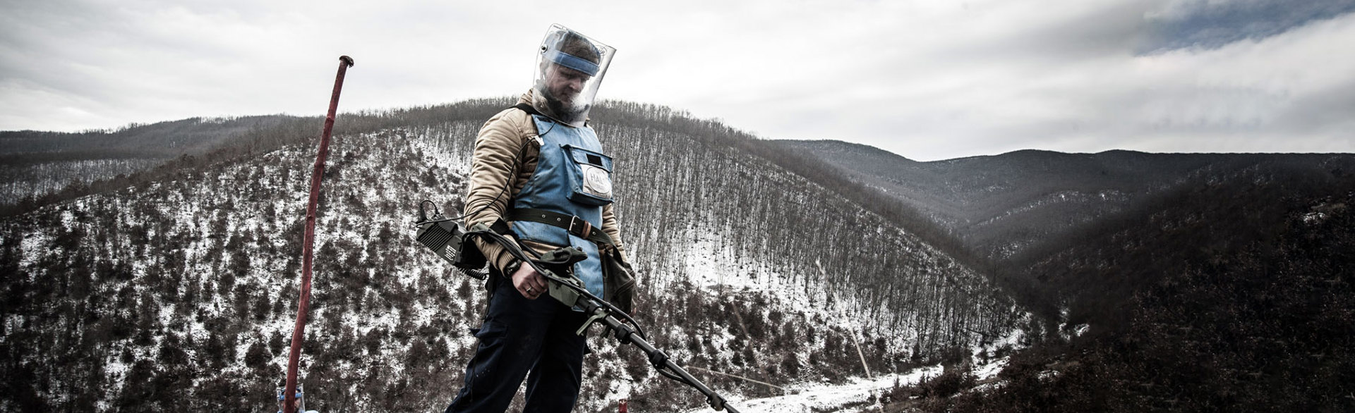 A deminer in Kosovo holds a detector whilst standing on a snow covered hill