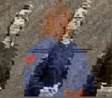 Портрет експертки з інформування про мінну небезпеку в синьому светрі зі знаком "MINES" на фоні стіни будівлі