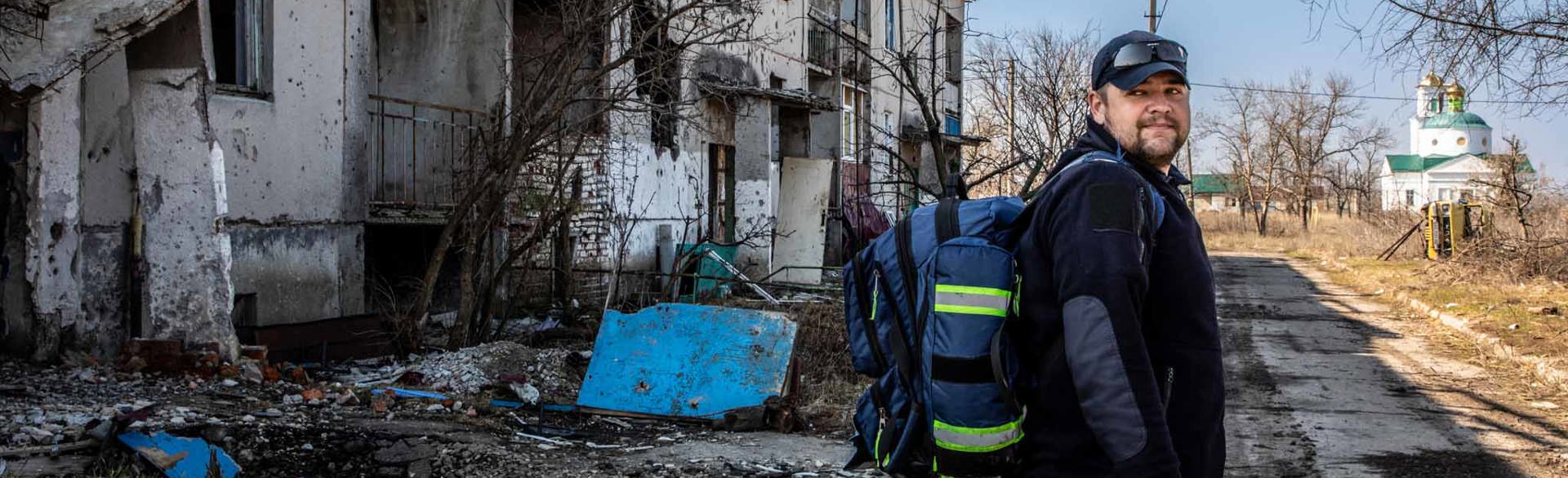 Спеціаліст ХАЛО під час проведення нетехнічного обстеження на фоні розбитих будівель