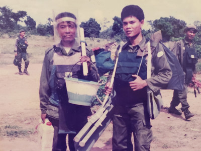 Two deminers in Cambodia wearing PPE and carrying equipment in a field in Cambodia