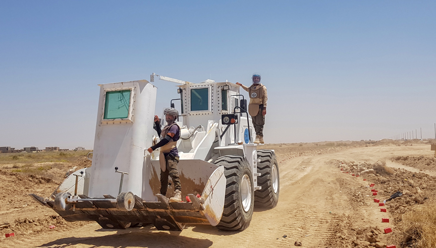 HALO staff ride a front loader used for mechanical clearance on a dusty track