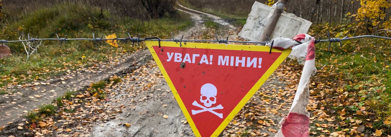 A red mine warning sign marks a muddy path into a field
