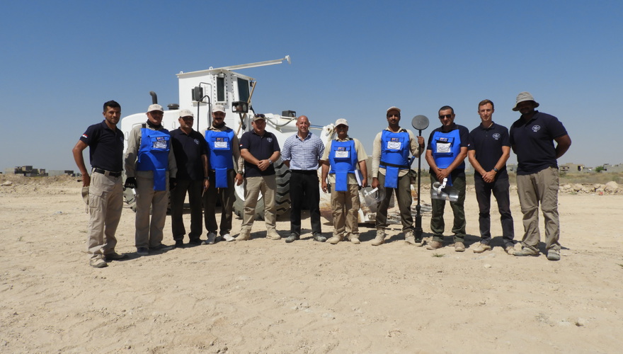 A group of HALO Staff stand in front of a mechanical asset in a desert in Iraq
