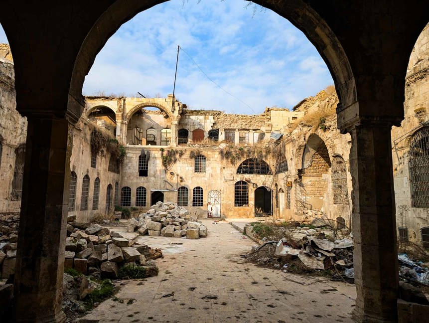 An archway leads to a courtyard of damaged buildings and rubble