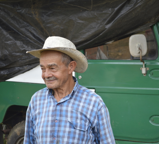 A Colombian farmer smiles in front of a large jeep like vehicle