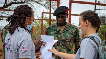 HALO staff members look at a piece of paper with military personnel outside