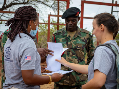 HALO staff members look at a piece of paper with military personnel outside
