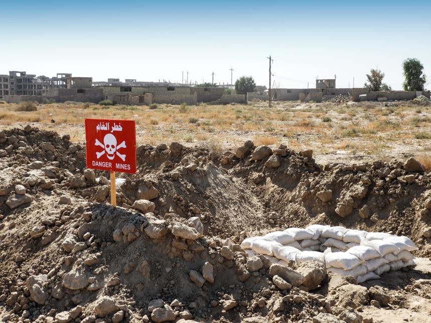 Mine warning sign with sandbags and destroyed buildings in the background 