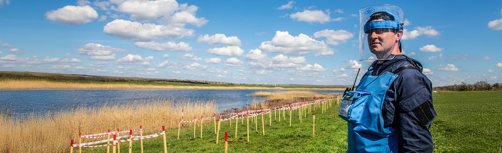 Демінер в захисному спорядженні на фоні маркування замінованої ділянки уздовж берега річки