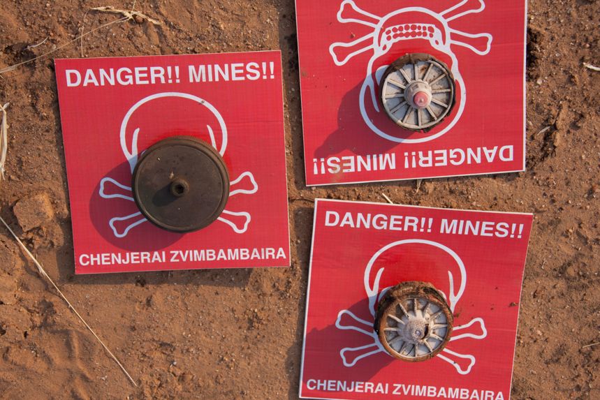 Mine warning signs lay on the soil with mines on top of them