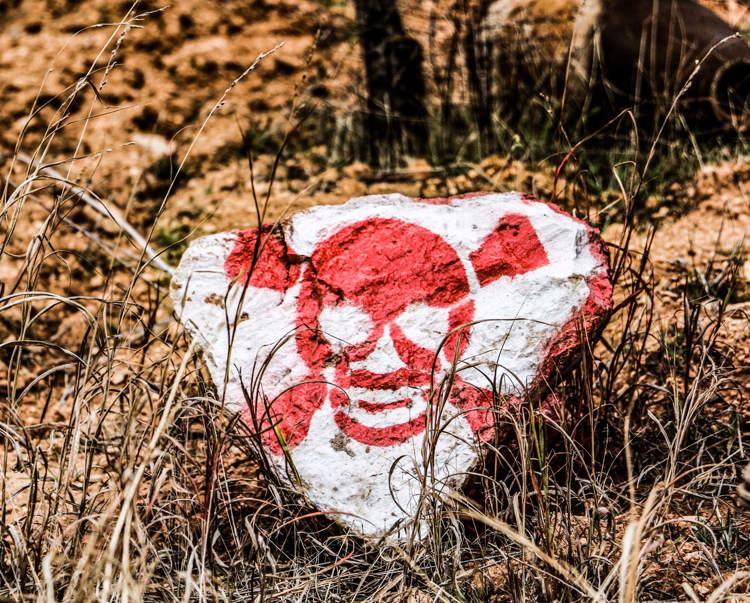 A rock painted with a skull and crossbones lies on the ground near explosive contamination in Syria