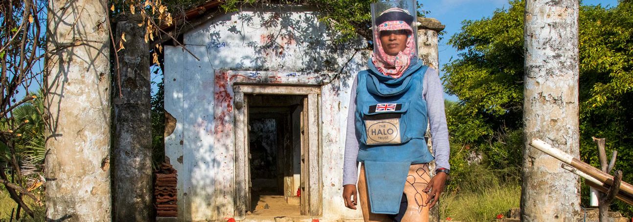A woman wearing PPE stands in front of an old building with pillars