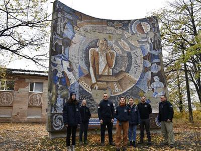 Команда НТО навпроти історичної мозаїки, що зображає радіооператора, оточеного астрономічними символами