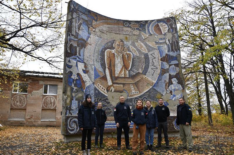 Команда НТО навпроти історичної мозаїки, що зображає радіооператора, оточеного астрономічними символами