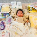 A baby lays on a soft mat with a blanket and maternal care items around them