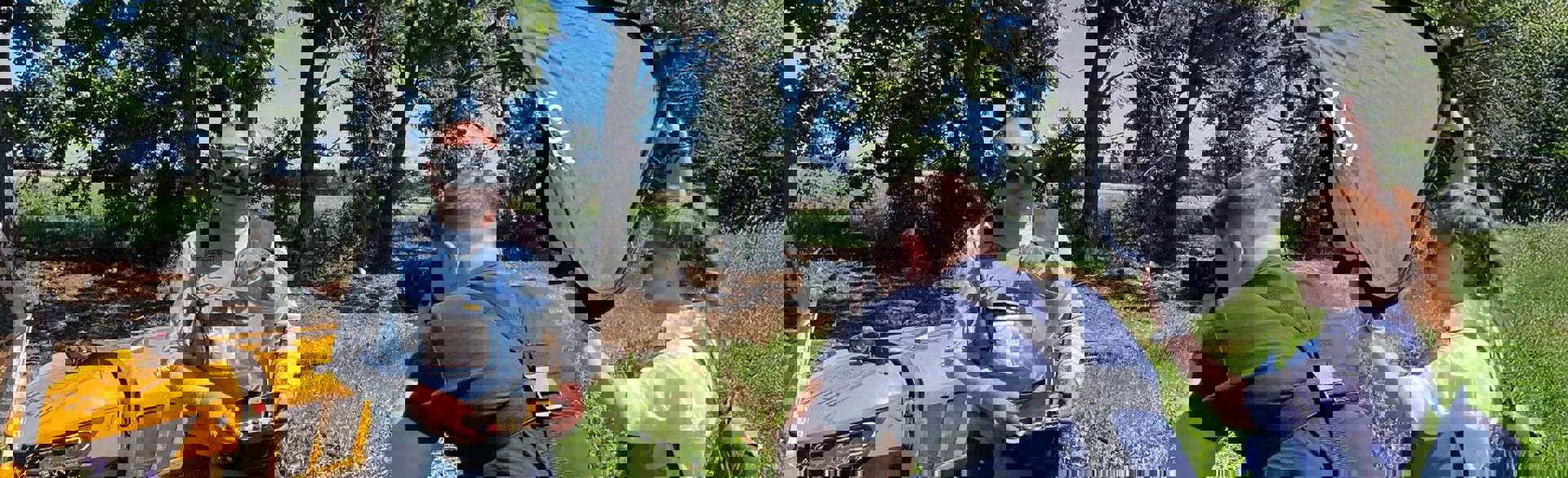 Журналісти фотографують демінера в захисному спорядженні з пультом керування від машини для дистанційної зрізки рослинності Robocut на фоні цієї машини біля лісопосадки