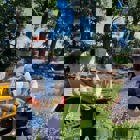 Журналісти фотографують демінера в захисному спорядженні з пультом керування від машини для дистанційної зрізки рослинності Robocut на фоні цієї машини біля лісопосадки