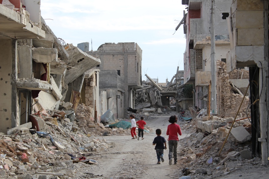 Children walk through streets filled with rubble and destroyed buildings either side