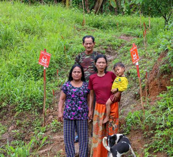 Cheng Seang and his family stand on grassy land marked with mine warning signs