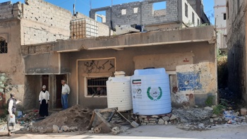 Three people stand in front of the rubble of a home in Taiz, Yemen.