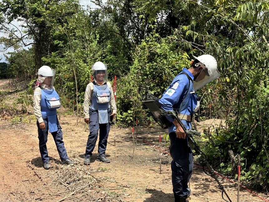 Ly Sreyneang and Pat Liv stand behind a HALO staff member using a metal detector to scan for mines